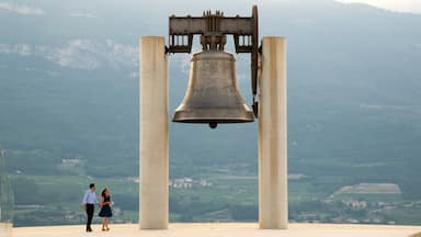 A large bell supported by four columns, with a mountainous landscape in the background.