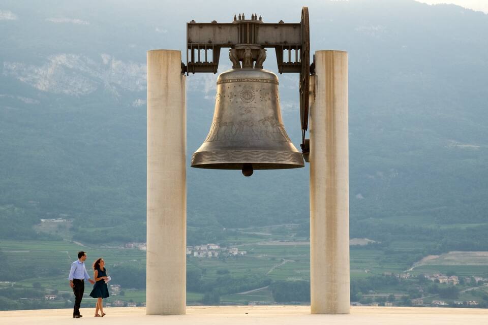 A large bell supported by four columns, with a mountainous landscape in the background.