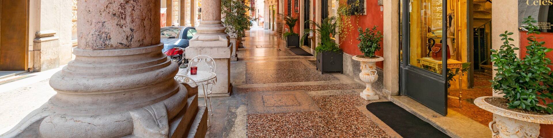 A cobblestone alley with classical architecture, including columns and arches, leading to a storefront with a glass door.