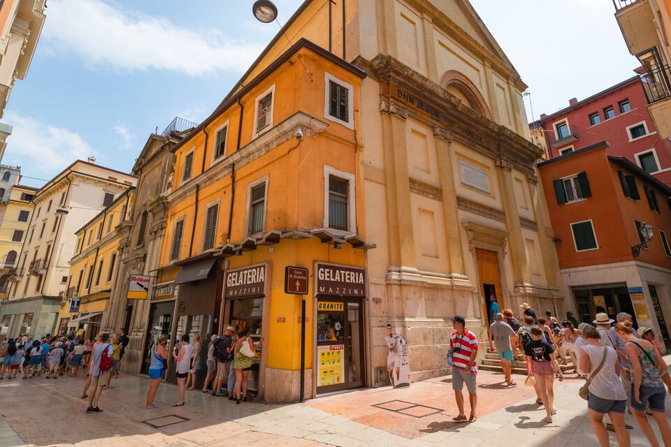 A bustling street with historic buildings, including a yellow building with a sign for Gelateria Mazzini.