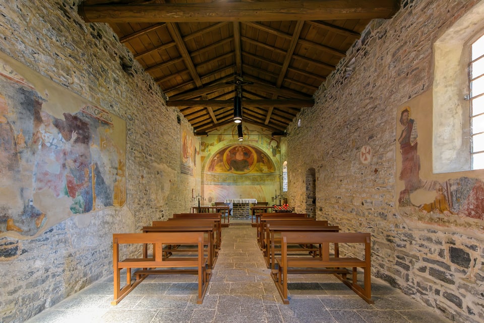 Interior de una iglesia con bancos de madera, paredes de piedra y frescos coloridos.