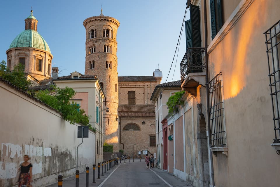 A narrow street with a church tower and a dome.