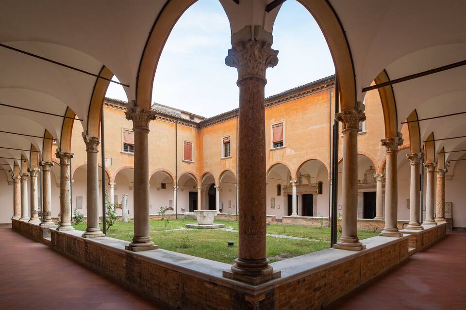 A courtyard with arches and columns, a grassy area, and a building with a tiled roof.