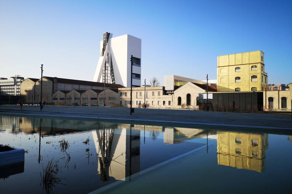 Un cos d'aigua tranquil·la que reflecteix edificis, incloent una construcció moderna blanca i un edifici groc.