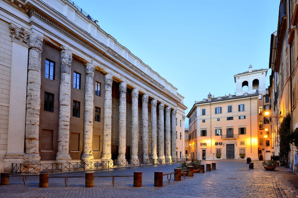 A cobblestone square with classical columns and a building with a bell tower.