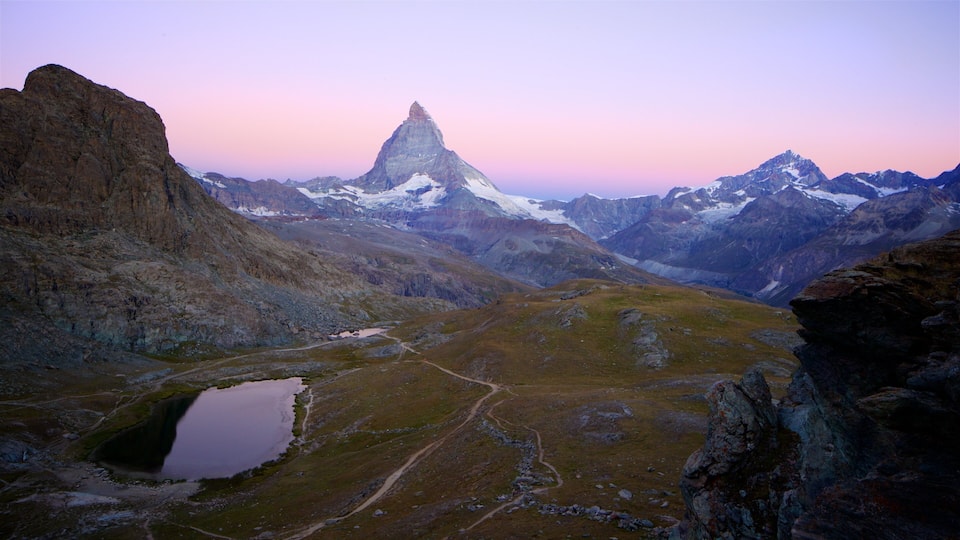 A mountainous landscape with a prominent peak, a small lake, and a winding path.