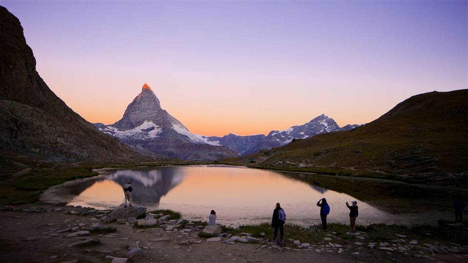 A group of people by a lake with a mountain in the background.