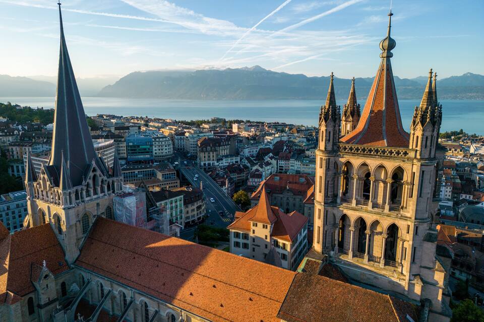A cityscape with prominent church spires, a river, and distant mountains.