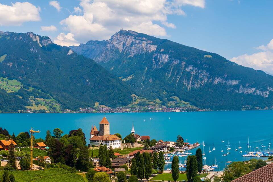 A lake surrounded by mountains, a church, and a marina with boats.