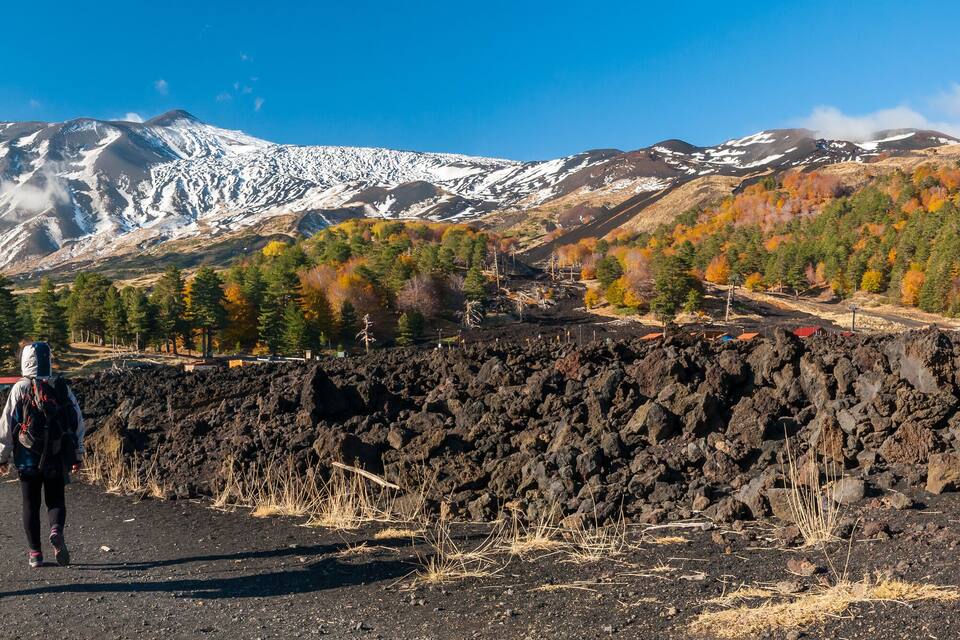 A mountainous landscape with a clear sky, a person walking on a path, and a pile of lava rocks.