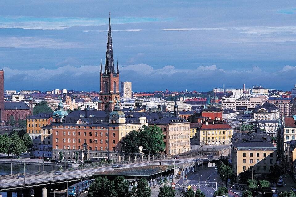 Un paisaje urbano con una destacada aguja de iglesia, un puente y un río.
