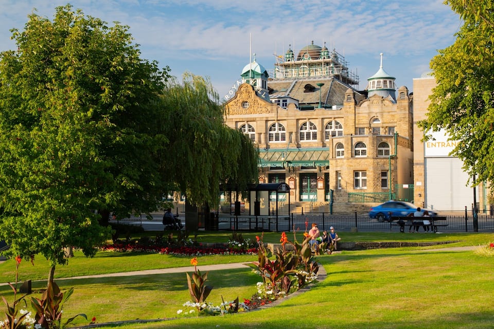 Un edificio storico con una cupola verde e una torre dell'orologio, circondato da vegetazione lussureggiante e un giardino curato.