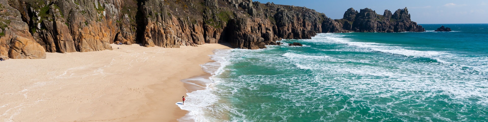 Uma praia arenosa com águas turquesa cristalinas e falésias rochosas.