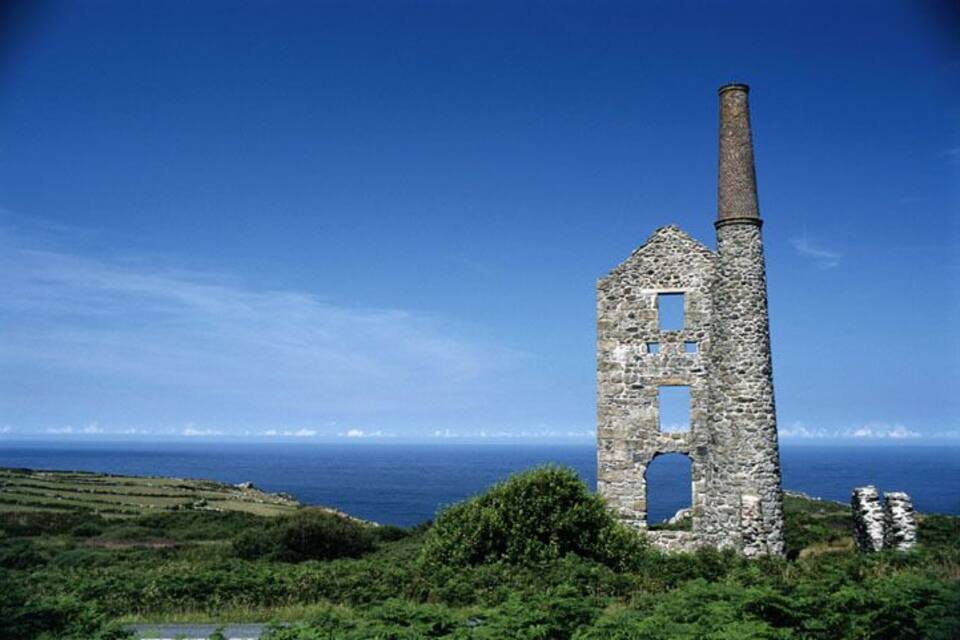 Rovine in pietra con un alto camino, immerse nel verde e con vista sull'oceano.