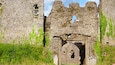 A medieval stone castle with ivy-covered walls, a large arched entrance, and a small window with bars.