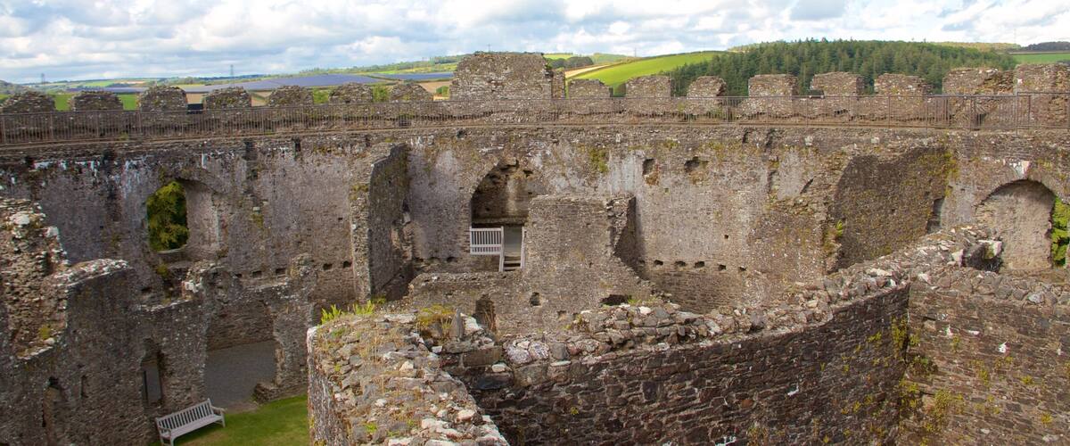 Ruinas de un castillo de piedra histórico con múltiples arcos y un área cercada.