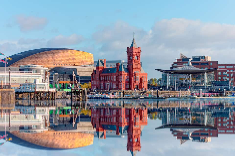 A waterfront cityscape with a large stadium, a red clock tower, and modern buildings.