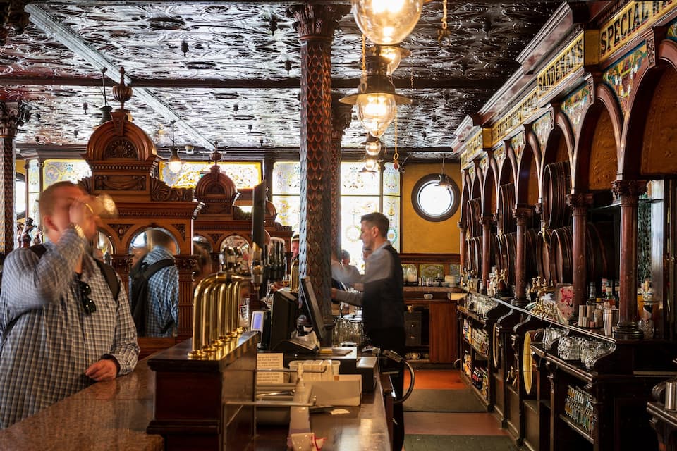 En detaljeret bar med træsøjler, en bartender og et udvalg af flasker.