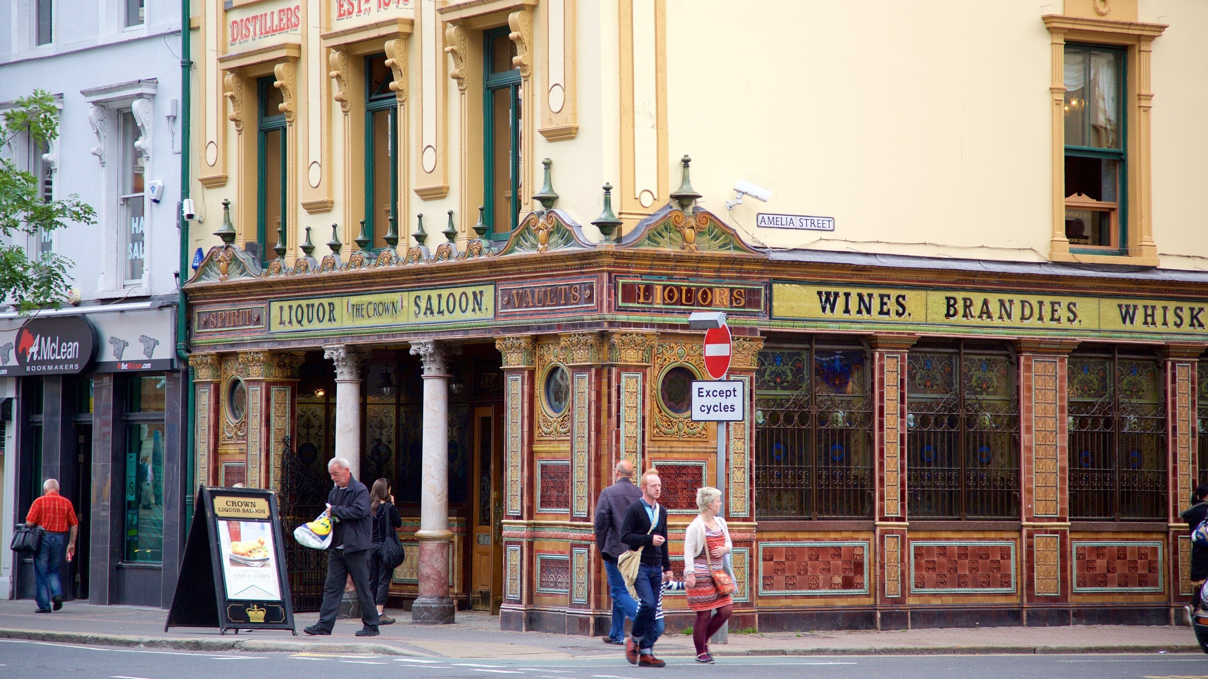 A historic building with ornate architecture, including columns and decorative moldings. The facade displays signs for 'Spirits', 'Liquor', 'The Crown', 'Saloons', 'Vaults', 'Liquor', 'Wines', 'Brandy', and 'Whiskey'.