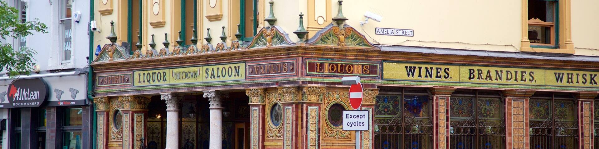 A historic building with ornate architecture, including columns and decorative moldings. The facade displays signs for 'Spirits', 'Liquor', 'The Crown', 'Saloons', 'Vaults', 'Liquor', 'Wines', 'Brandy', and 'Whiskey'.