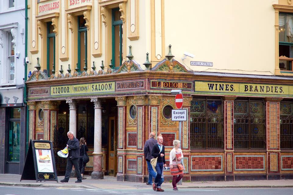 A historic building with ornate architecture, including columns and decorative moldings. The facade displays signs for 'Spirits', 'Liquor', 'The Crown', 'Saloons', 'Vaults', 'Liquor', 'Wines', 'Brandy', and 'Whiskey'.
