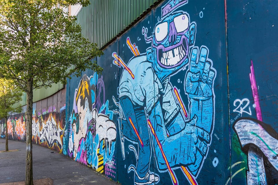 Ein farbenfrohes Graffiti-Mural an einer Wand mit Bäumen und einem Bürgersteig.