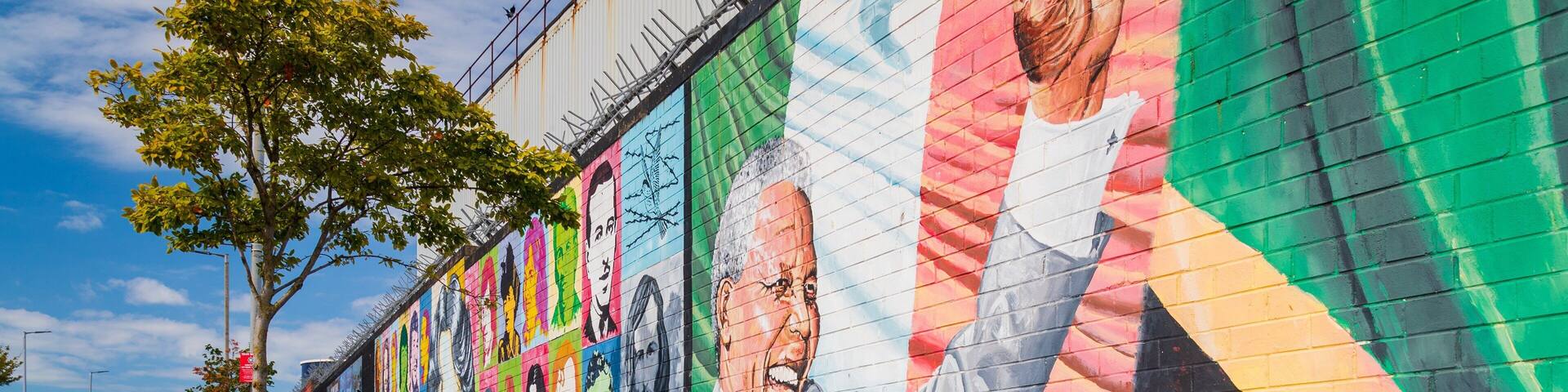 A colorful mural on a city wall with portraits and text.
