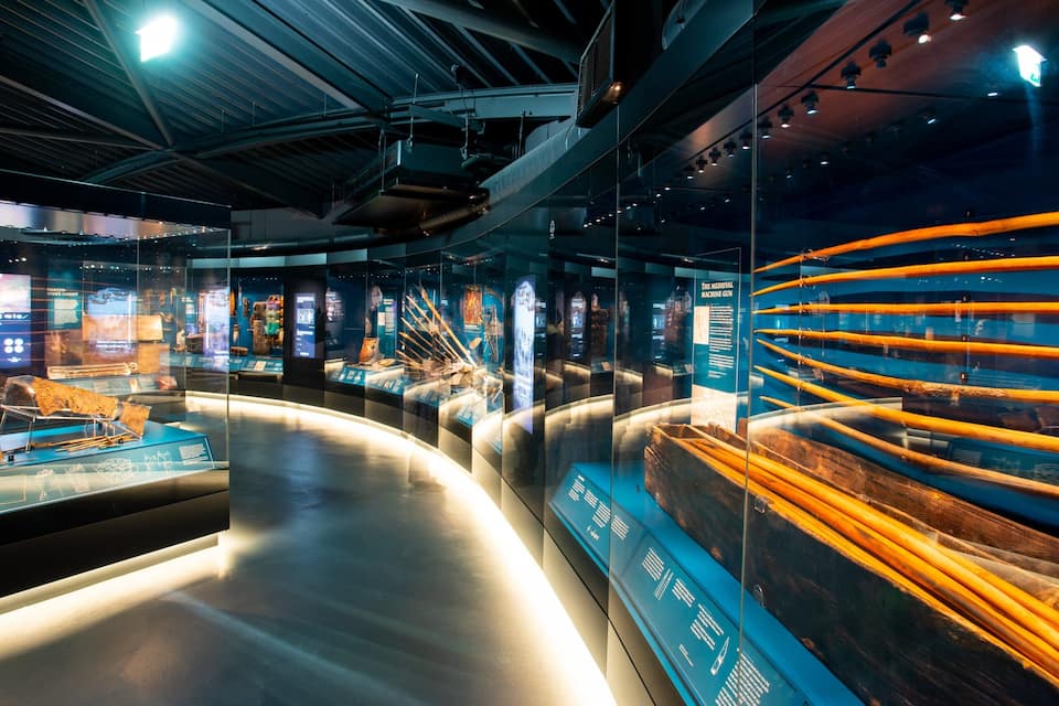 An indoor museum exhibit with glass display cases containing historical artifacts and information panels.