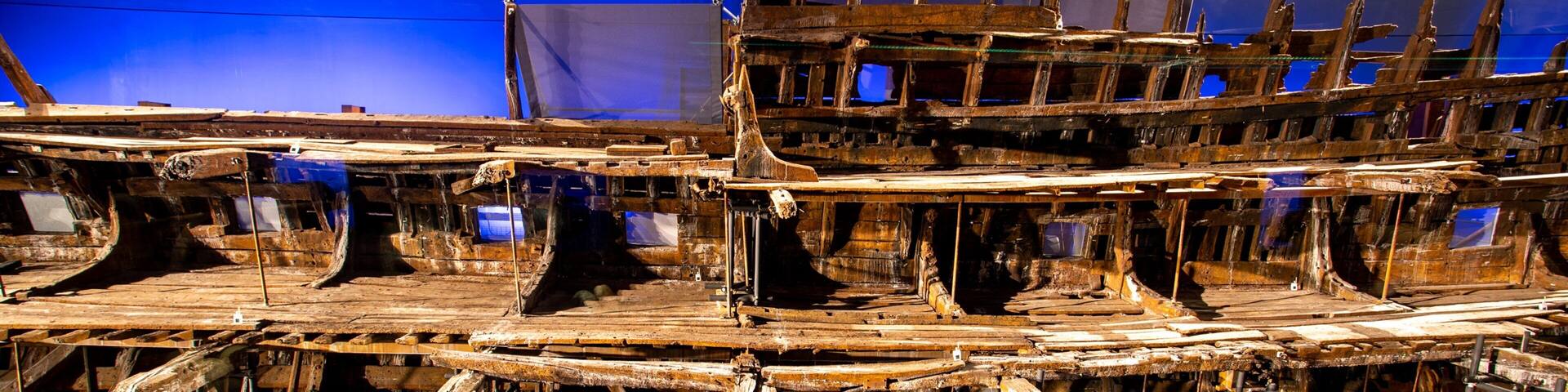 A large, intricate shipwreck with exposed wooden beams and metal structures, displayed in a museum setting.