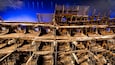 A large, intricate shipwreck with exposed wooden beams and metal structures, displayed in a museum setting.