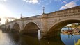 Un pont de pierre à arches multiples enjambant une rivière, avec des bateaux amarrés le long de la rive.