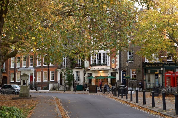 A tree-lined street with buildings, a pub named 'The Cricketers', and red telephone booths.