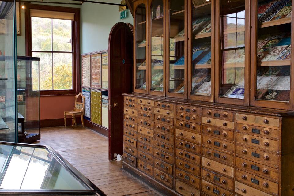 A wooden filing cabinet with glass doors and drawers, a chair, and a window with a view of trees.