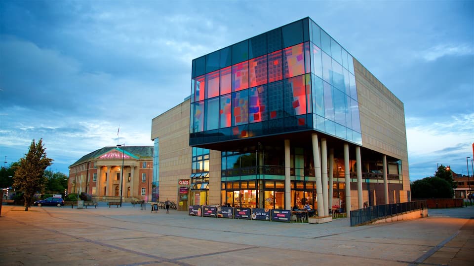 A modern building with large glass windows and a classical building in the background.