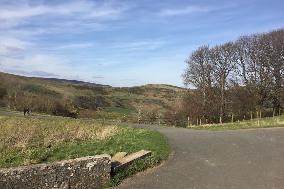 A rural road winding through a hilly landscape with sparse trees and a clear sky.