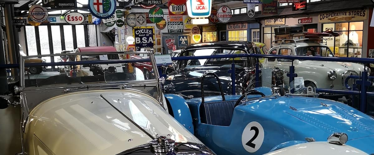 Vintage cars in a showroom with various brand signs like Pratts Motor Oil and Ford.