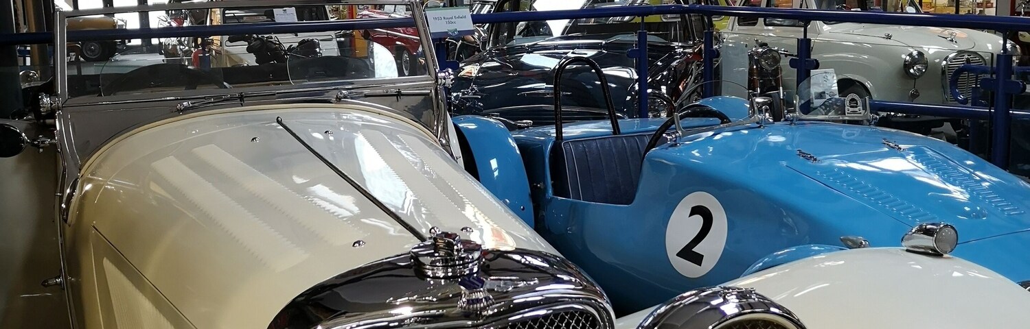 Vintage cars in a showroom with various brand signs like Pratts Motor Oil and Ford.