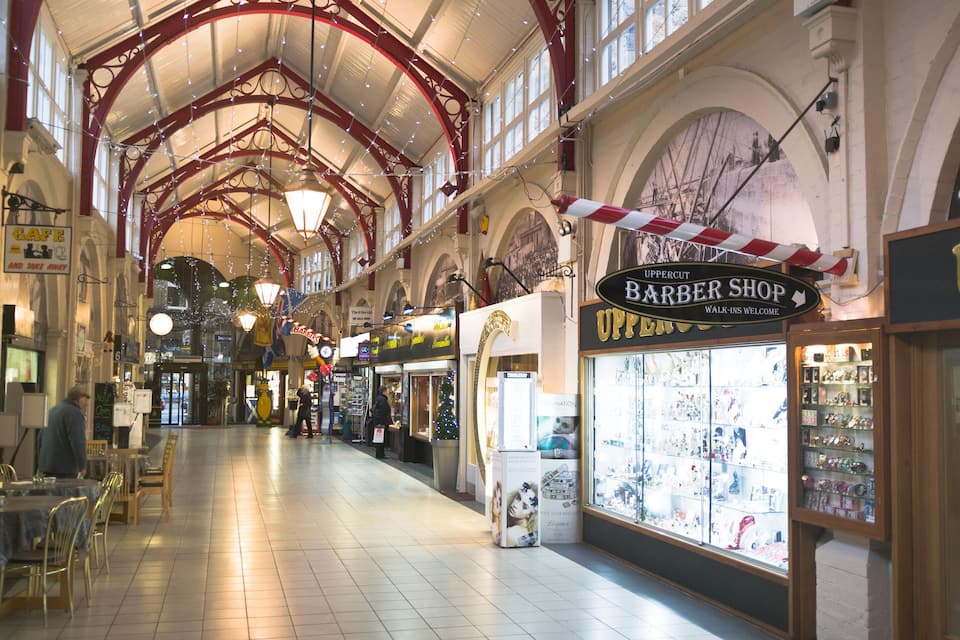 A spacious indoor market with a high arched ceiling, various shops including a barber shop, and a Christmas tree.