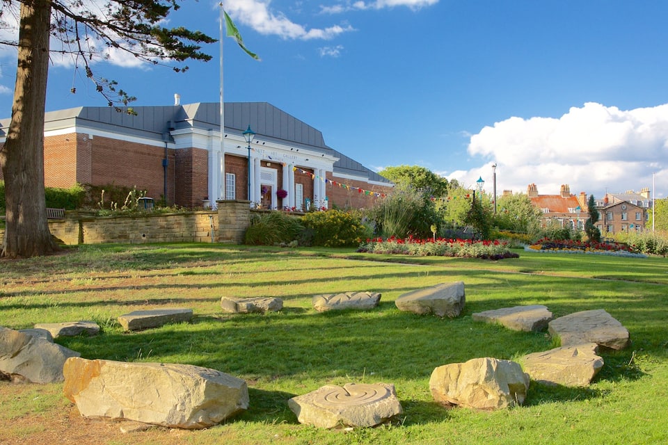 A landscaped garden with large rocks, a brick building labeled 'Nettl Art Gallery', and a clear blue sky.