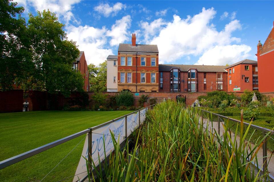 A row of red brick houses with a green lawn and a metal fence in the foreground.