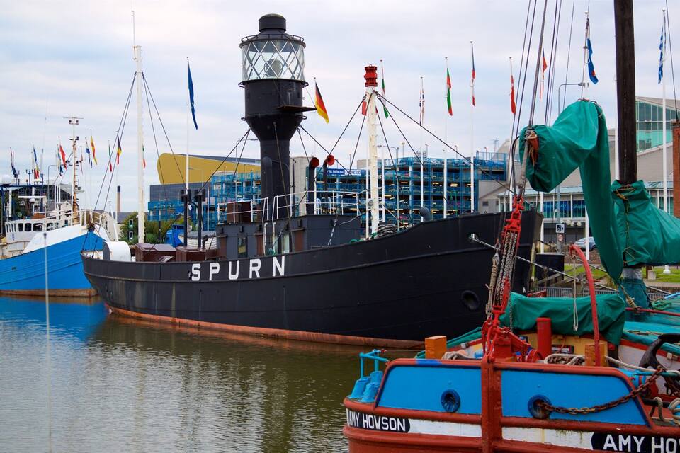 A large black ship named SPURN docked at a harbor with multiple flags and a building in the background.
