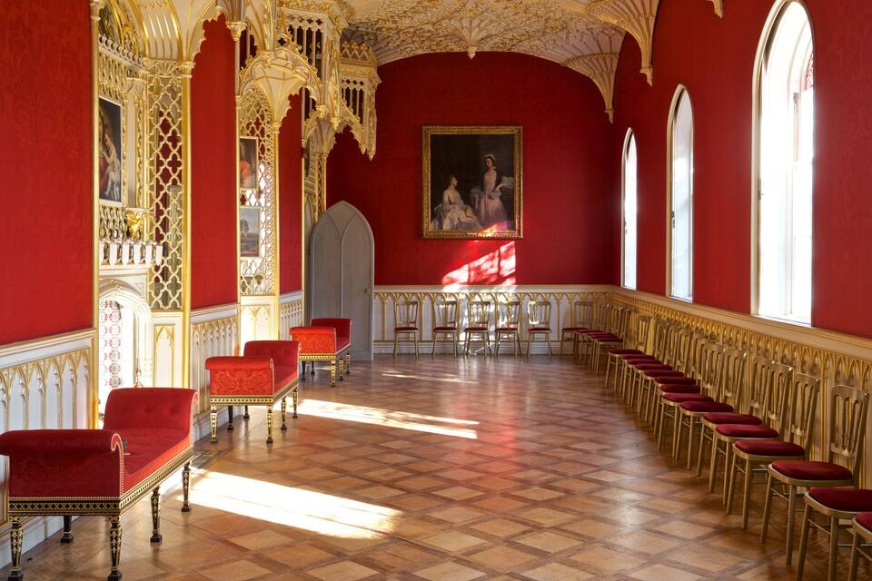 A grand hall with red walls, ornate gold detailing, and a checkered floor.