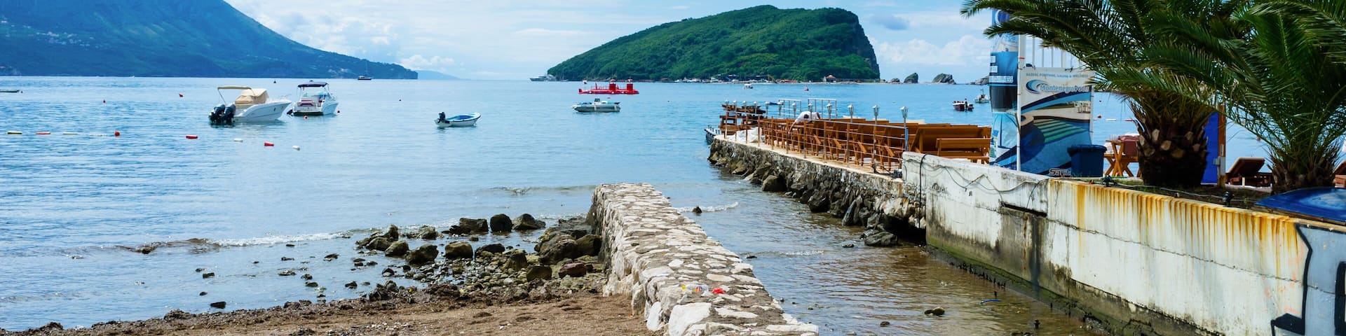 Un paysage côtier avec des bateaux, un mur de pierre et un palmier.