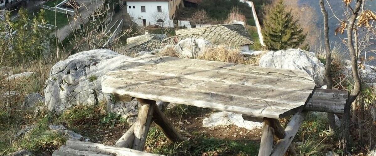 A wooden bench overlooking a valley with a house and a river.