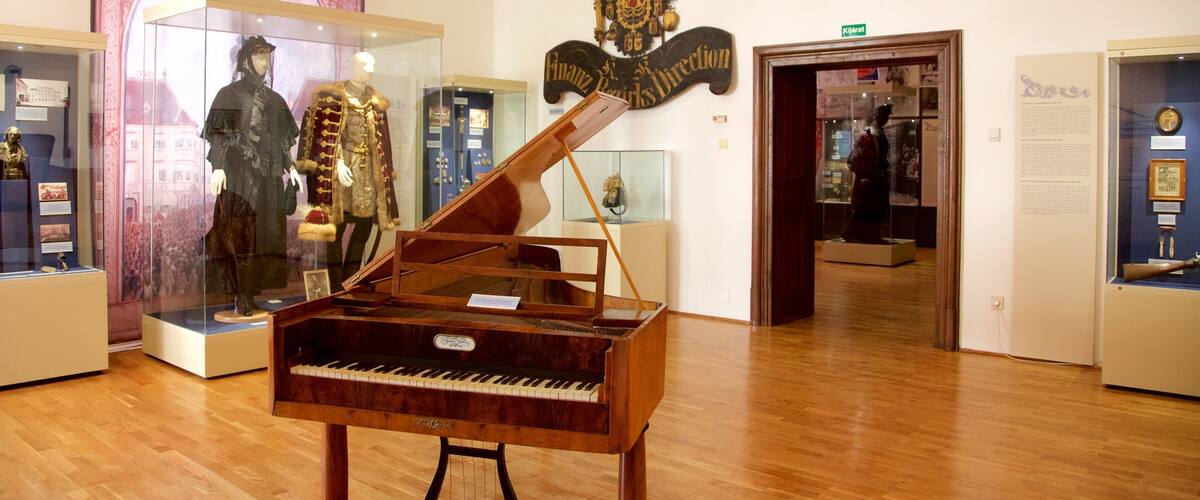 A grand piano in a museum with historical exhibits in the background.