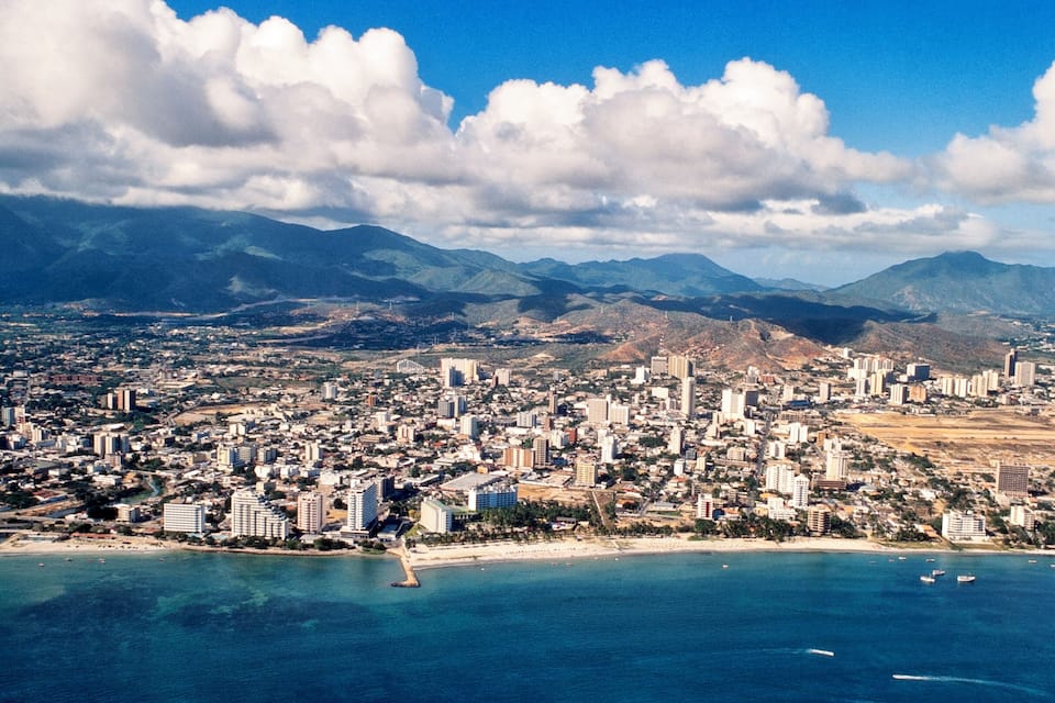 A coastal city with a beach, mountains, and a clear sky.
