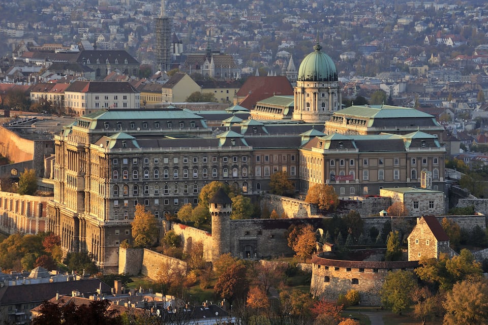 Un complesso di edifici storici con una cupola imponente e numerose torri, circondato da un'area fortificata e dal fogliame autunnale.