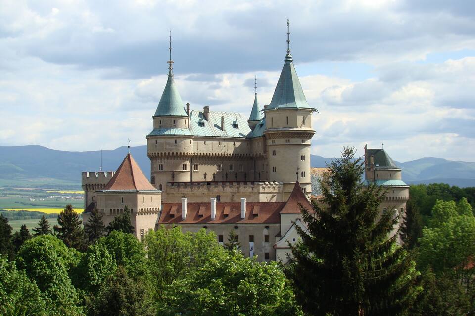 A castle with multiple towers and a large courtyard surrounded by trees.