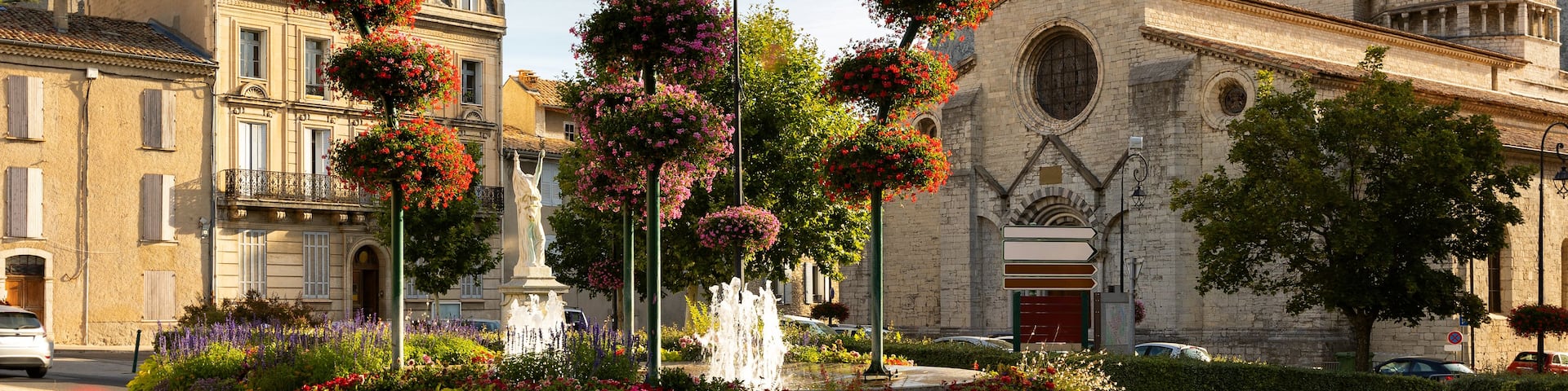 A historic church with a bell tower, surrounded by colorful flower baskets and a fountain.