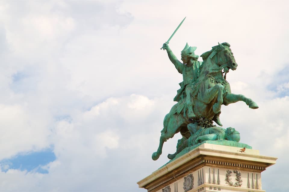 Une statue équestre en bronze, posée sur un piédestal et surmontée d’un oiseau, se détache sur un ciel nuageux.